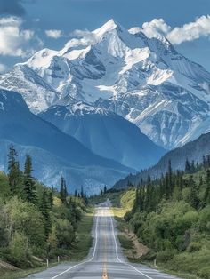 an empty road in the mountains with snow capped mountains on either side and trees lining both sides