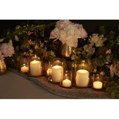 many lit candles are lined up on a table with flowers and greenery in the background