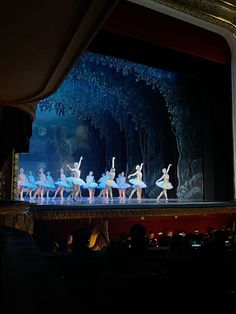 dancers on stage in front of an audience at a ballet performance with trees and blue lighting