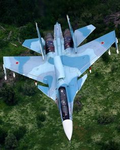 an aerial view of a fighter jet flying in the sky over green grass and trees