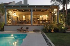 a house with a swimming pool in front of it and lights shining on the patio