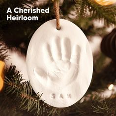 a white ornament hanging from a christmas tree with a handprint on it