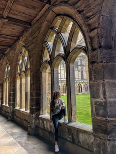 a woman sitting on a window sill in an old building looking out at the grass