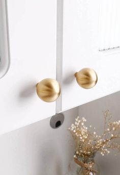 two gold knobs on the side of a white door and vase with baby's breath flowers