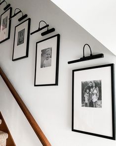 black and white photos hang on the wall above stairs with wooden handrails below