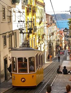 people sitting on the ground in front of a yellow trolly car going down a city street