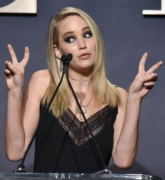 a woman standing at a podium with her hands in the air and making peace signs