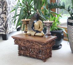 a buddha statue sitting on top of a wooden table in front of potted plants