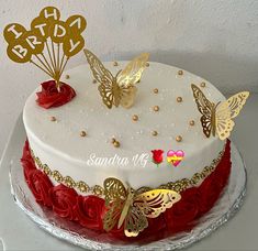 a birthday cake decorated with gold butterflies and red roses