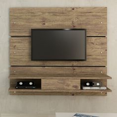 a tv mounted to the side of a wooden wall with shelves below it and a remote control