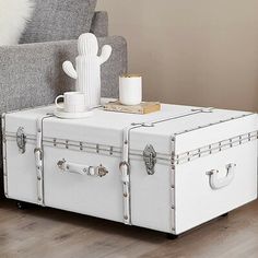 a white trunk coffee table sitting on top of a wooden floor next to a gray couch