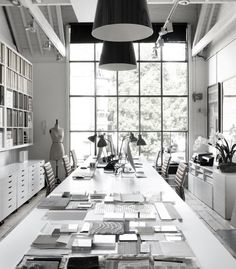 a long table with lots of books on it in front of large windows and shelves