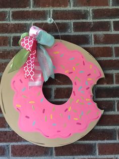 a pink doughnut with sprinkles and a bow hanging on a brick wall