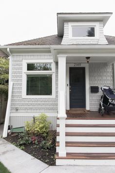 a baby stroller sits on the front steps of a white house with brown trim