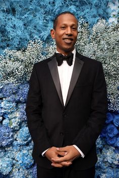 a man in a tuxedo standing in front of a blue flowered wall