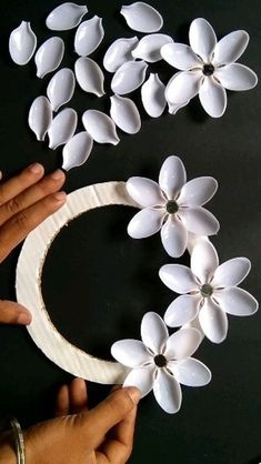 two hands are holding white paper flowers on a black surface