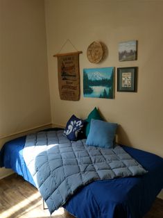 a bed with blue comforter and pillows in a bedroom next to pictures on the wall