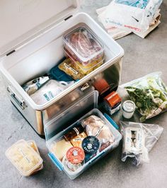 an open lunch box sitting on the ground next to other food and condiments