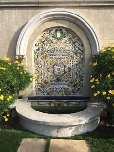 an ornate fountain surrounded by yellow flowers and greenery