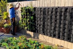 a man is using a garden hose to clean up the plants in his back yard