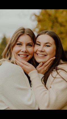 two women hugging each other in front of trees