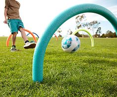 a person kicking a soccer ball on top of a green grass covered field next to an arch