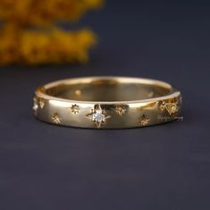 a gold wedding band with stars and diamonds on the side, sitting next to a yellow flower