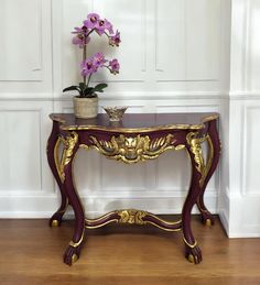 a purple and gold console table with flowers in a vase on it's top