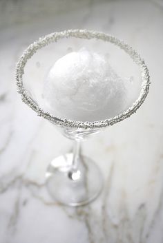 a glass filled with white liquid on top of a marble countertop next to a silver spoon