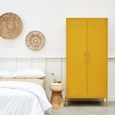 a yellow locker sitting next to a bed in a room with two baskets on the wall