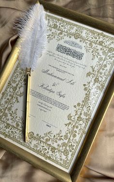 an ornate wedding card with a feather resting on it's side next to a pen