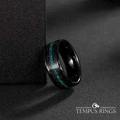 a black ring with blue and green inlays sitting on top of a table