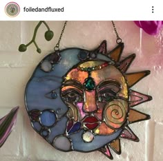 a sun face hanging on a wall with beads and other things around it, including flowers