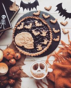 a table topped with cookies and other halloween treats next to a cup of coffee on top of a plate