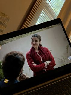 a laptop computer with a woman on the screen and another person in the background looking at her