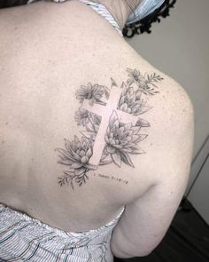 the back of a woman's shoulder with a cross and flowers tattoo on it