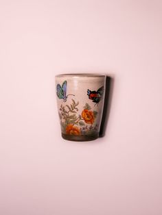 a white cup with flowers and butterflies painted on the side, hanging from a wall