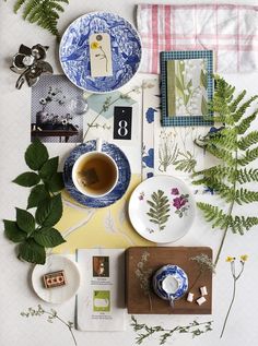 the table is set with plates, cups and flowers on it as well as other items