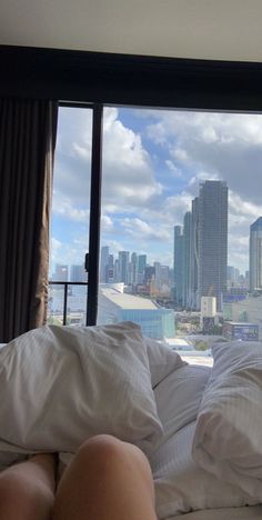 a woman laying on top of a bed in front of a window with city view