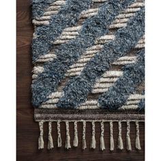 a blue and white rug with tassels on top of wooden flooring next to a wall