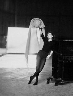 a black and white photo of a woman in tights leaning on a luggage cart