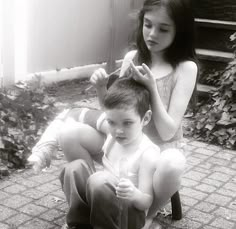 a young boy sitting next to a woman who is combing her hair in black and white