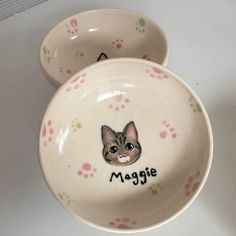 two ceramic bowls with designs on them sitting next to each other, one has a cat's face painted on it