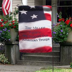 an american flag on a pole in front of a house with flowers and potted plants