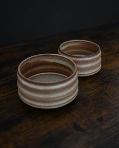 two small brown bowls sitting on top of a wooden table next to eachother