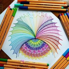 some colored pencils are laying on top of a white paper with an intricate design