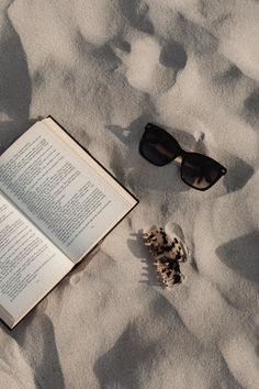 an open book and sunglasses on the sand