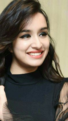 a woman with long hair smiling and wearing a black top on her shoulders is looking at the camera