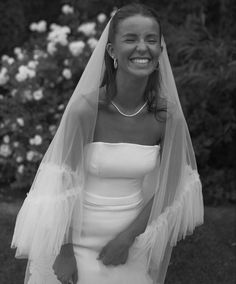 a woman in a wedding dress and veil smiles at the camera while posing for a black and white photo