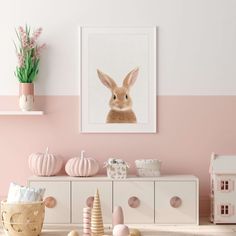 a pink and white room with a rabbit on the wall next to a dresser in front of it